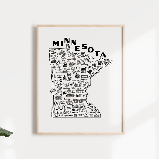 A black and white print of a hand-illustrated map of Minnesota state with various icons, displayed in a simple wood frame, accompanied by a green potted plant to the side.