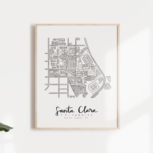 A framed black and white print of Santa Clara University campus map, displayed against a wall with foliage around it.