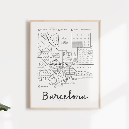 Black and white map print of Barcelona, Spain, framed and displayed against a wall with foliage around it.
