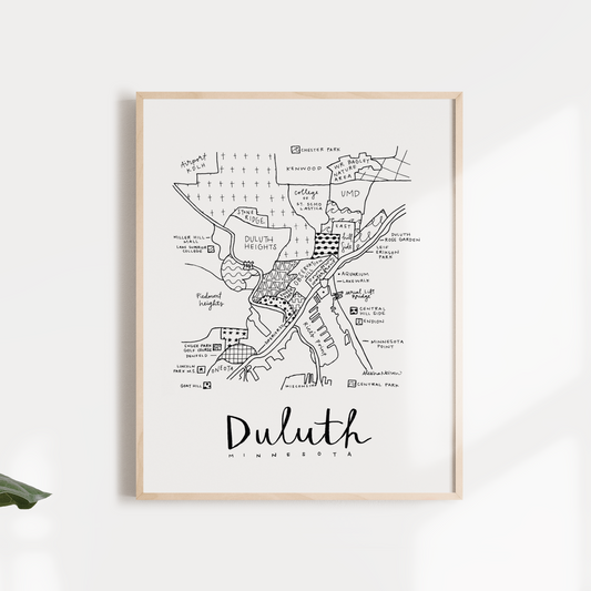 Black and white map print of Duluth, MN, framed and displayed against a white wall with green leaves in the foreground.