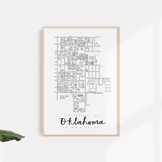 Black and white print of a hand-illustrated map design of the University of Oklahoma, framed and displayed against a white wall with green foliage surrounding it.