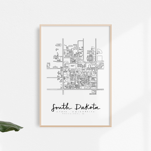 Black and white print of South Dakota State University campus map, framed and displayed on a wall with foliage in the foreground.