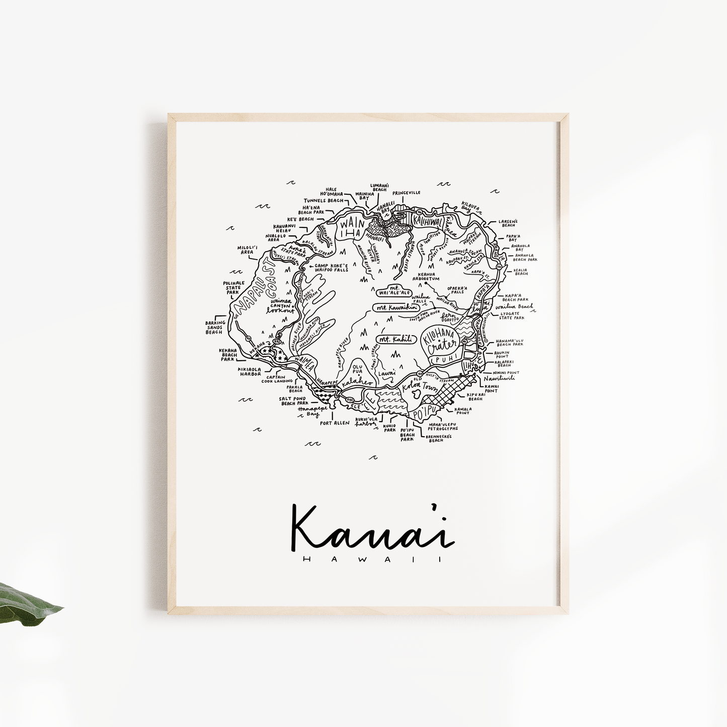 Framed map of Kauai, Hawaii on a white wall with green leaves.