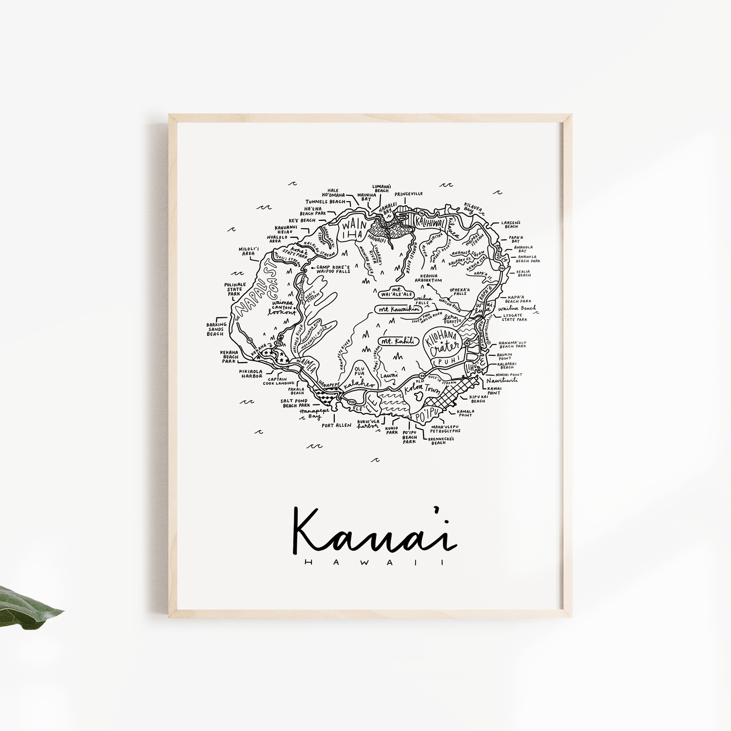 Framed map of Kauai, Hawaii on a white wall with green leaves.