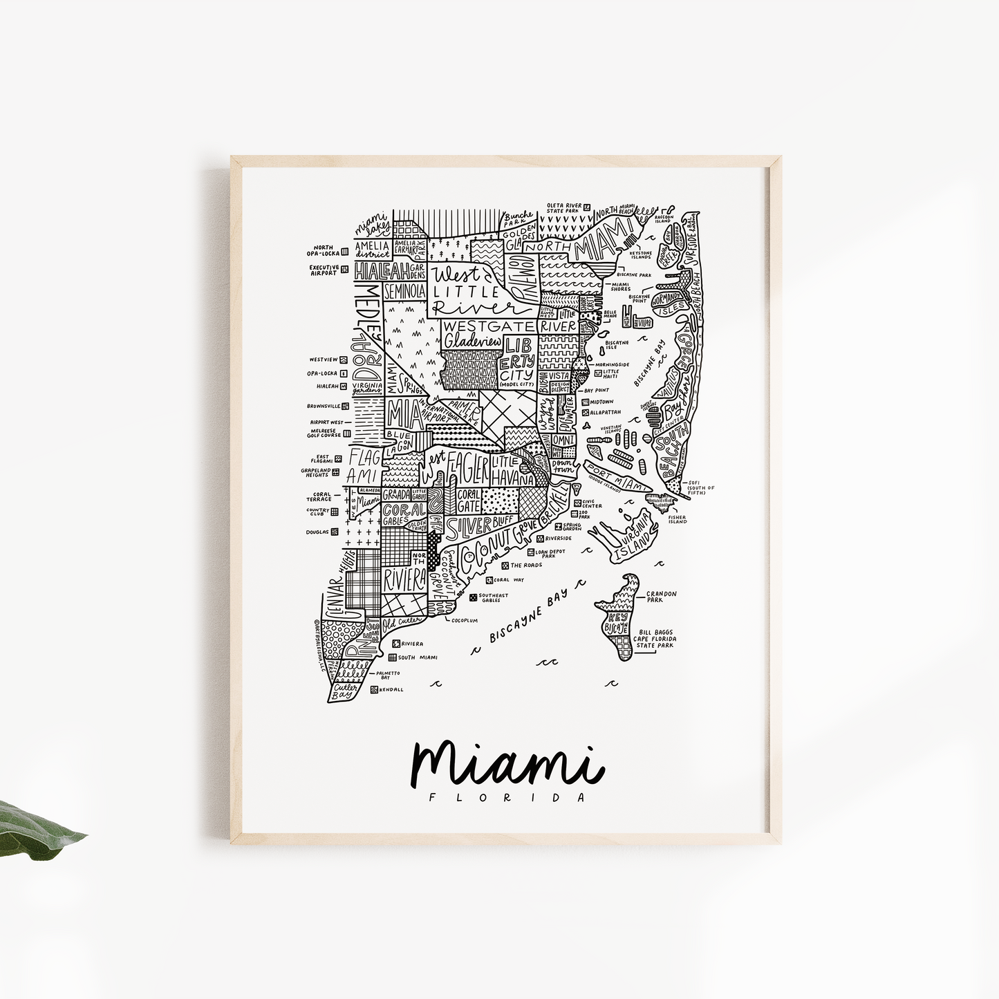 Framed map of Miami on a white wall with green leaves.