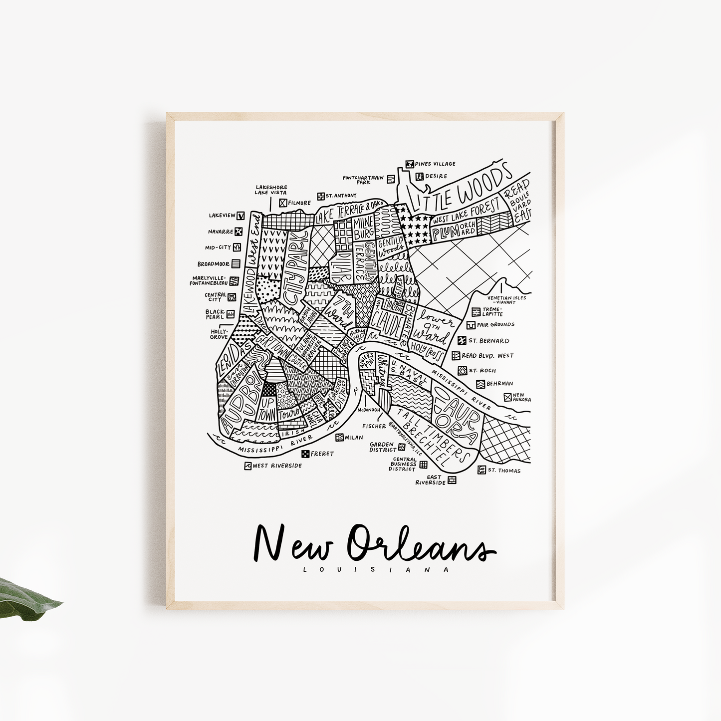 A framed black and white street map print of New Orleans, Louisiana, displayed on a clean white wall with decorative green leaves on the sides.