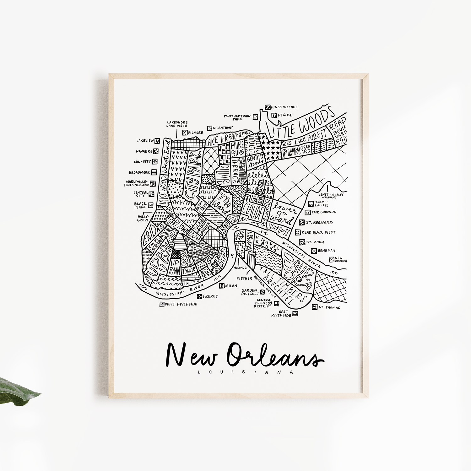 A framed black and white street map print of New Orleans, Louisiana, displayed on a clean white wall with decorative green leaves on the sides.