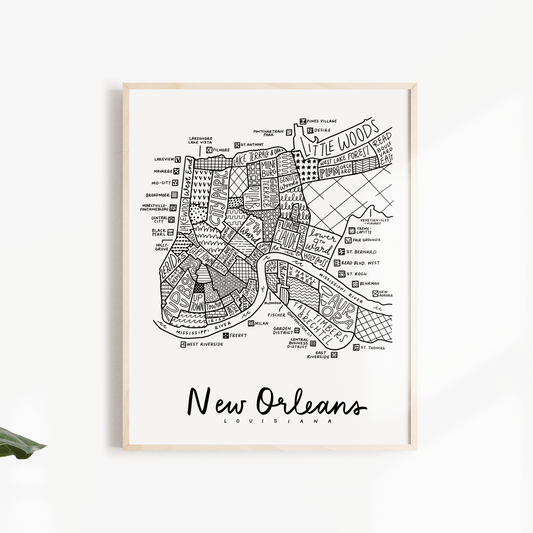 A framed black and white street map print of New Orleans, Louisiana, displayed on a clean white wall with decorative green leaves on the sides.
