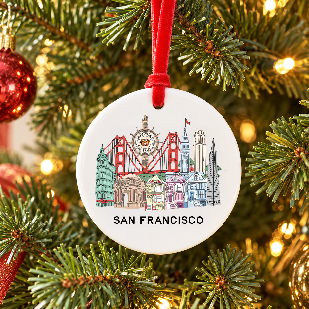 A round white Christmas ornament featuring a colorful illustrated skyline of San Francisco with the text 'SAN FRANCISCO' at the bottom, hanging from a red ribbon on a decorated Christmas tree.